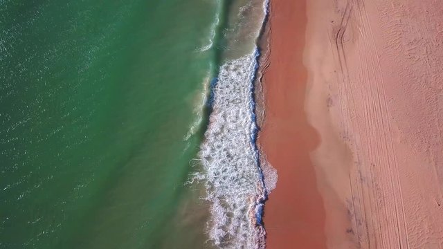 Aerial overhead shot over waves reaching a sand beach.