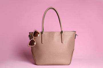 Stylish woman's bag and sunglasses on light pink background