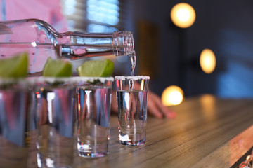 Bartender pouring Mexican Tequila into shot glasses at bar counter, closeup