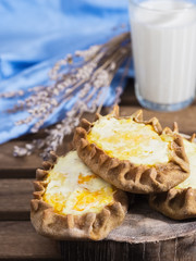 Karelian Pirakka pies located on a wooden stand. In the background is a glass of milk. Traditional dish of Karelia and Finland from rye flour with different fillings. Close-up