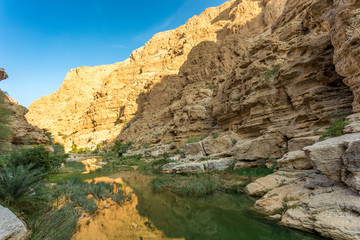 Fototapeta na wymiar Wadi Shab river canyon with rocky cliffs and green water springs - Sultanate of Oman