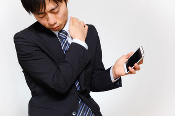 肩こりに悩むスーツ姿の男性　血行不良　スマートフォン