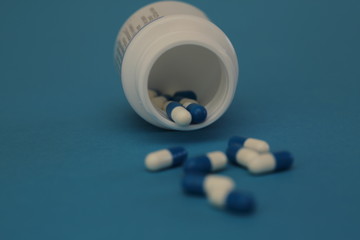 Capsules tablets in open pharmaceutical bottle, in front other pills in soft focus, blue background, close up