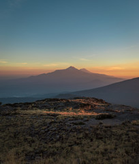 Naklejka premium Meksykańskie wulkany o zachodzie słońca w pomarańczowych kolorach i błękitnym niebie, Popocatepetl i Iztaccíhuatl