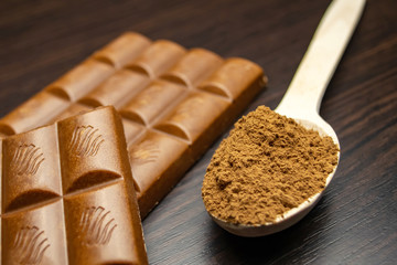 Chocolate and wooden spoon with cocoa on a black background