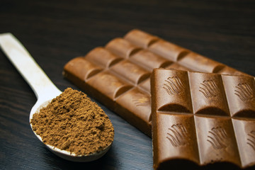 Chocolate and wooden spoon with cocoa on a black background