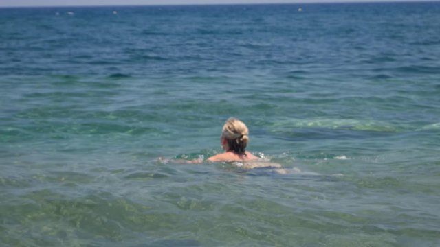 Blonde Scandinavian Woman Swims In The Ocean of Santorini in Greece To Cool Off The Warm Weather, Handheld Wide Shot