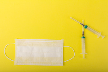 White medical mask and medical syringe isolated on yellow background. Face mask protection against pollution, virus, flu and coronavirus.