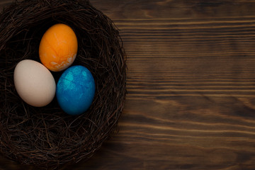 Hand painted dark blue, orange and white easter eggs in nest on rustic wooden background