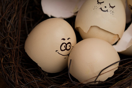 Eggs with funny faces in nest on wooden table. Happy easter egg concept.