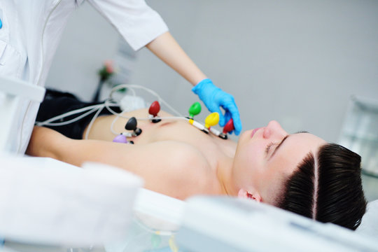 a young male patient in a modern clinic checks the state of the heart and makes an ECG or electrocardiogram with vacuum rubber colored sensors electrodes on the chest. 