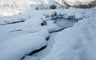 Fototapeta na wymiar Frozen mountain river brook in the snow on beautiful snowy winter