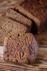 A loaf of black rye homemade bread lies on a wooden table.