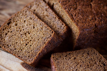 A loaf of black rye homemade bread lies on a wooden table.