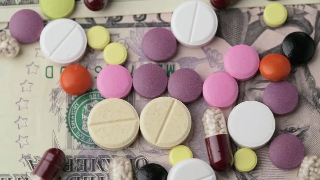 The concept of making money on medicines. Multicolored drugs on a background of dollars. Different remedy, pills, capsule, antibiotic and vitamin rotate.