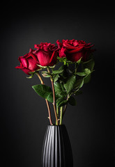 Beautiful bouquet of red roses in a black vase. Black background. Close-up. Vertical format.