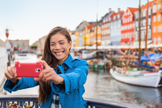 Copenhagen travel selfie Asian tourist woman taking selfie picture photo as souvenir with smartphone camera in the old port Nyhavn, famous Scandinavian attraction in Denmark, northern Europe.