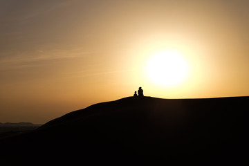 A boy and a man in Arabic national costumes look at the landscape in the RUB al-Khali desert . Silhouettes against a sunset in the desert
