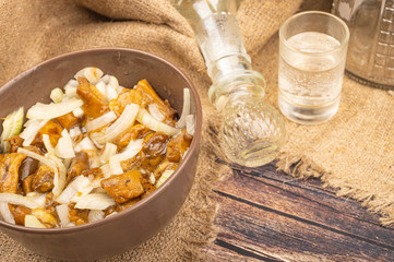 Pickled mushrooms with onions in a ceramic bowl , a glass of vodka and a decanter on a background...