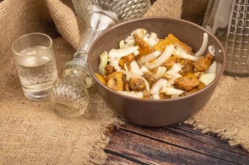Pickled mushrooms with onions in a ceramic bowl , a glass of vodka and a decanter on a background of rough homespun fabric.. Homemade preparations, Rustic treats. Close up.