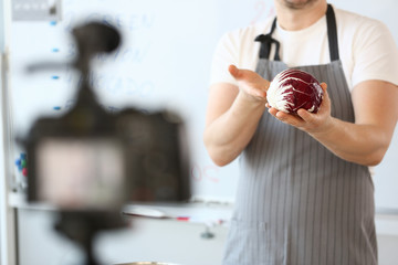 Male Vlogger Hands Holding Purple Organic Cabbage. Cook in Apron Recording Culinary Vlog on Camera at Kitchen. Fresh Ingredient for Vegetarian Food. Round and Ripe Cole. Healthy Food Recipe.