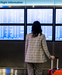 Young woman in international airport looking at the flight information board. Traveler checking gate information