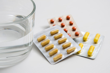 Pills and glass of water on white background.