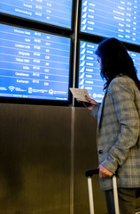 Young woman in international airport looking at the flight information board. Traveler checking gate information