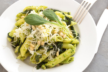 Penne pasta with spinach on grey background.