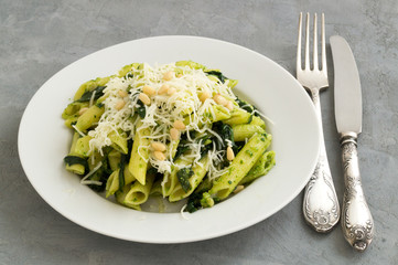 Penne pasta with spinach on grey background.