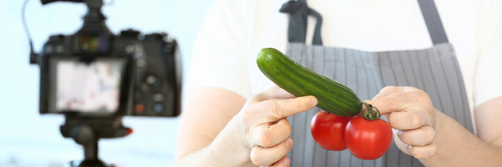 Chef Vlogger Holding Tomatoes Cucumber Humorously. Man Joking with Vegetable Penis. Funny Culinary Vlog. Man Recording in Kitchen at Home on Camcorder. Cuisine with Healthy Organic Food