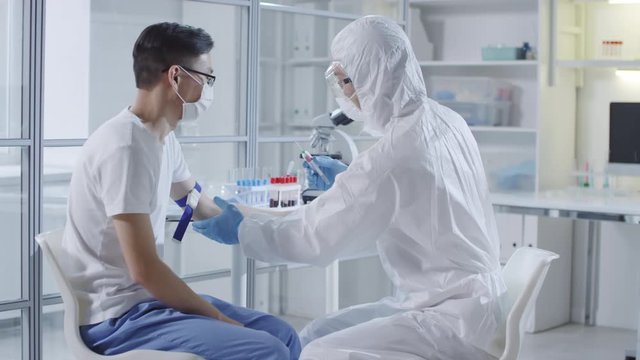 Tracking of unrecognizable doctor or medical scientist in protective suit, gloves, mask and goggles injecting sick Asian patient with experimental vaccine from coronavirus