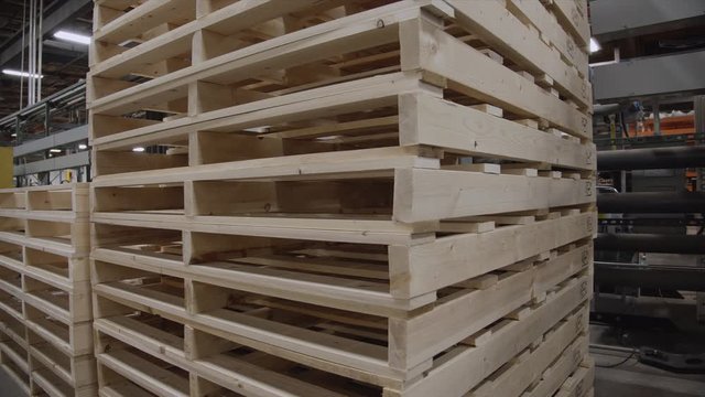 Medium slider pan of stacked wooden pallets inside a factory. Pipes, metal and industrial lights in the background. Perfect for manufacturing or shipping projects.