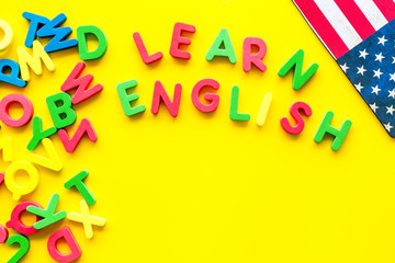 Learn English text near American flag and letters on yellow background top-down copy space