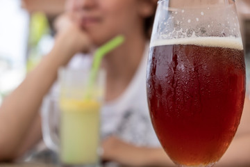 Fototapeta premium Closeup of cold red ale in glass with unfocused woman drinking beverage.