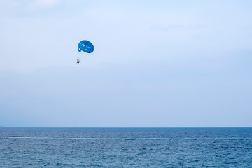 Parasailing water amusement - flying on a parachute behind a boat on a summer holiday.  Tourist with parasailing on ocean sea with blue sky background.