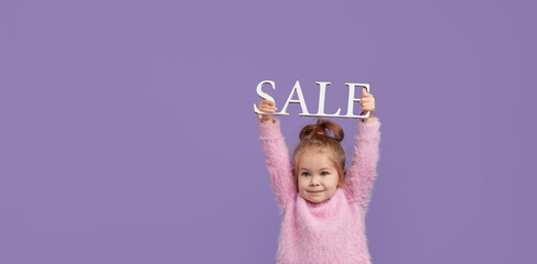 Sale of childrens products. Portrait of fun little child girl  on purple background holding shopping bags, package. Looking at the camera. Banner. Space for text.