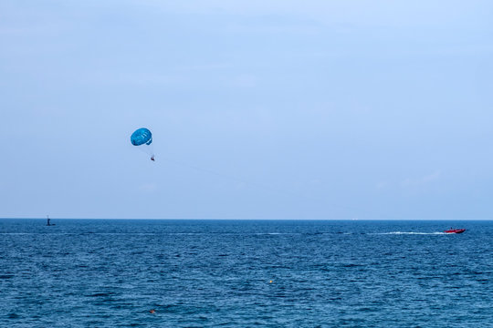 Parasailing water amusement - flying on a parachute behind a boat on a summer holiday.  Tourist with parasailing on ocean sea with blue sky background.