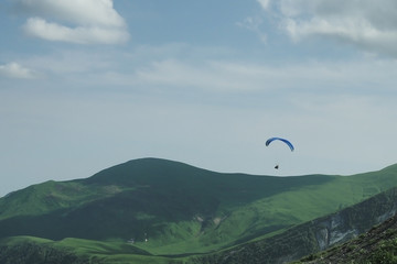 Paraglider flying over mountains in summer day