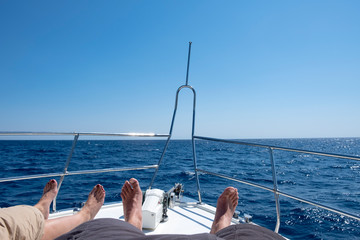 Couple feet on sailboat front in sunny day. View on man and woman legs laying on yacht with blue sea. Summer holidays concept.