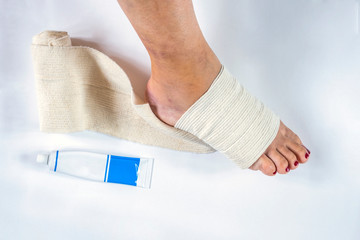 Woman is wrapping her leg with sprained ankle with elastic bandage isolated on white background. Twisted bandaged ankle and gel on white background.  Athlete runner is applying gel after  training acc