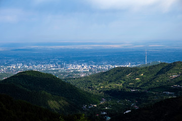 Fototapeta premium Beautiful view to Almaty city and foothills with storm clouds captured from mountains. Green almaty mountains foothills clouds in beautiful style on blue background.