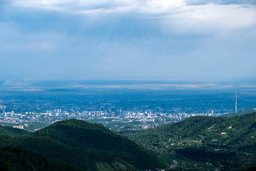 Fototapeta na wymiar Beautiful view to Almaty city and foothills with storm clouds captured from mountains. Green almaty mountains foothills clouds in beautiful style on blue background.