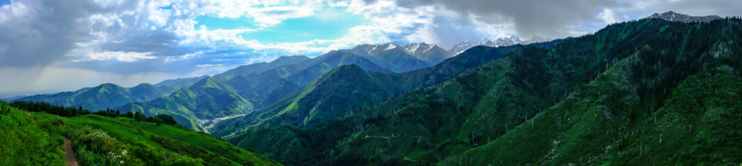Panoramic landscape of Almaty mountains with cloudy stormy clouds. Overcast - weather storm. Rain in mountains.