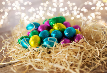 Fototapeta na wymiar easter, confectionery and holidays concept - chocolate eggs in foil wrappers in straw nest on wooden table