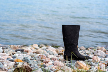 Rubber boot of sunk fisherman laying on the coast. Sunk person concept. Nature disaster. Save water concept. Sea swimming.
