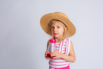 a little girl in summer clothes and a bottle of juice with a straw on a white background. The concept of summer vacation