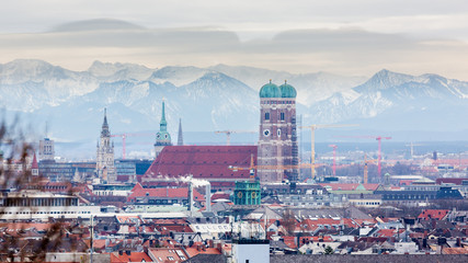 Munich, Bavaria / Germany - Feb 20, 2020: Frauenkirche with snow-capped alps (mountains) in the background. Symbol & landmark of the bavarian capital. Beautiful panorama captured during winter season. - obrazy, fototapety, plakaty