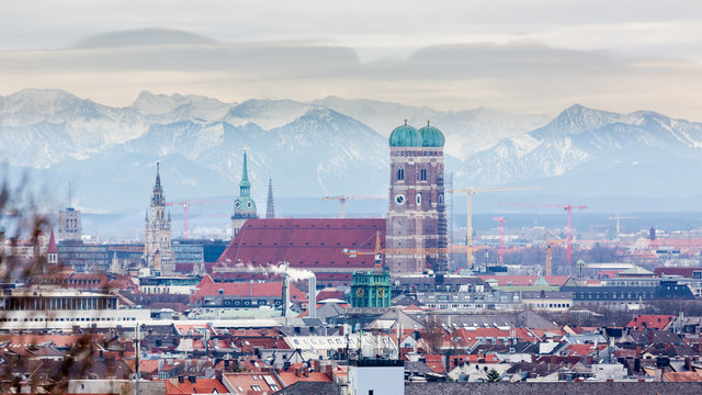 Munich, Bavaria / Germany - Feb 20, 2020: Frauenkirche with snow-capped alps (mountains) in the background. Symbol & landmark of the bavarian capital. Beautiful panorama captured during winter season.