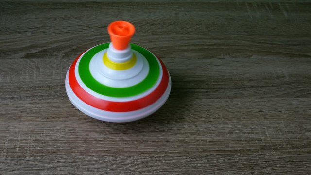 Multicolored plastic spinning top or whirligig top is traditional toy for preschool childs. Rotates in circle on wooden surface. Boys and girls with pleasure watching them spin. Close-up.